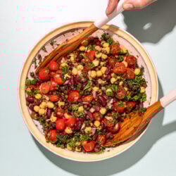 hands tossing bean salad with wooden spoons